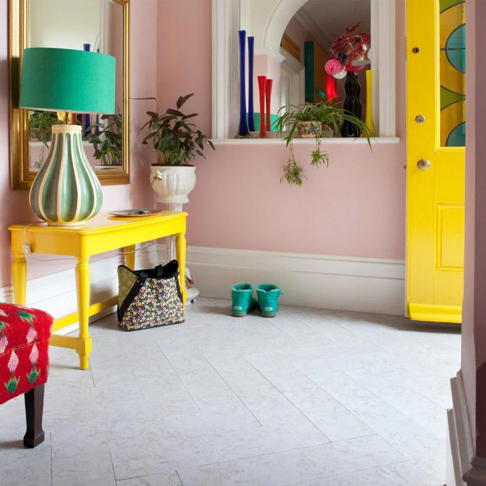 A cheerful entryway with pink and yellow walls, featuring a stylish table and a warm lamp, complemented by distinctive cork flooring