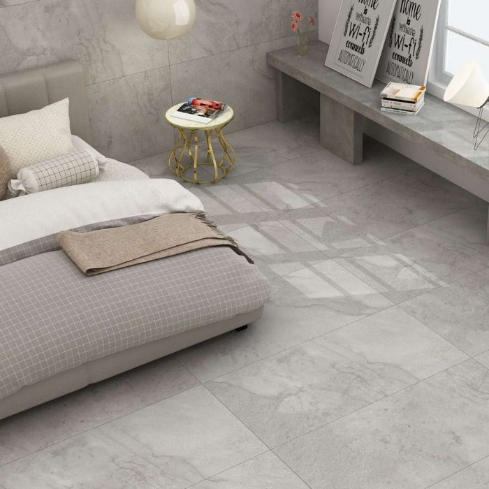 Modern bedroom with grey tiled floors, featuring a neatly made bed and stylish bedside table