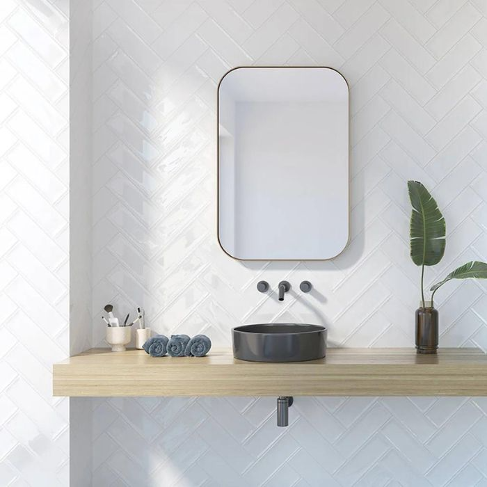 A bright white bathroom featuring pristine herringbone tiles, a sleek sink, and a stylish mirror