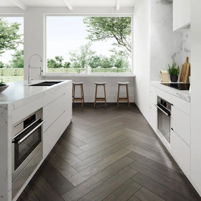 Modern kitchen featuring white cabinets, wooden floors, and a window overlooking greenery