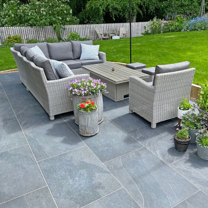 Inviting patio space with grey wicker furniture and lush green plants on garden tiles