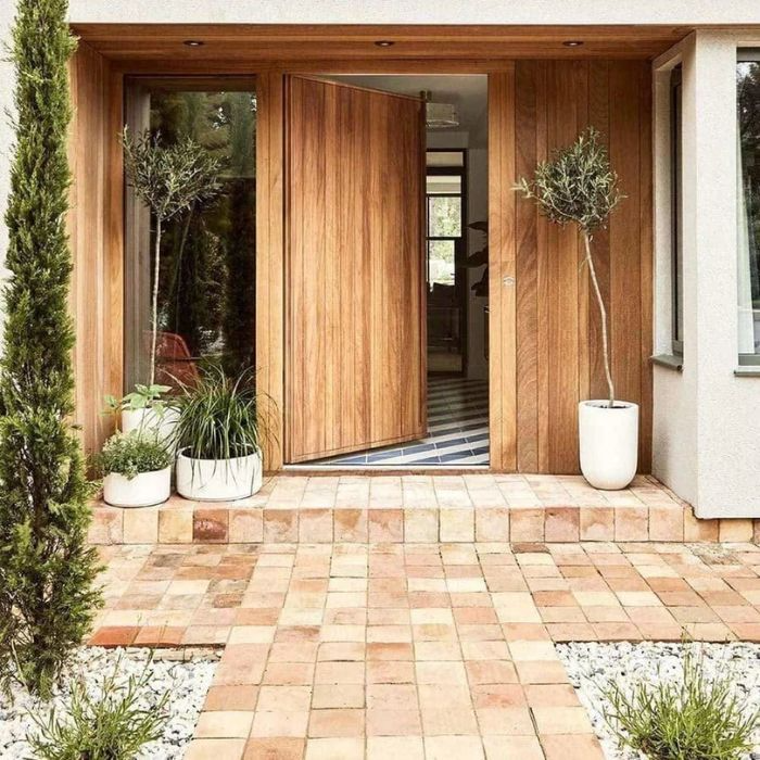 A charming entryway featuring a wooden door surrounded by vibrant potted plants and decorative porch tiles