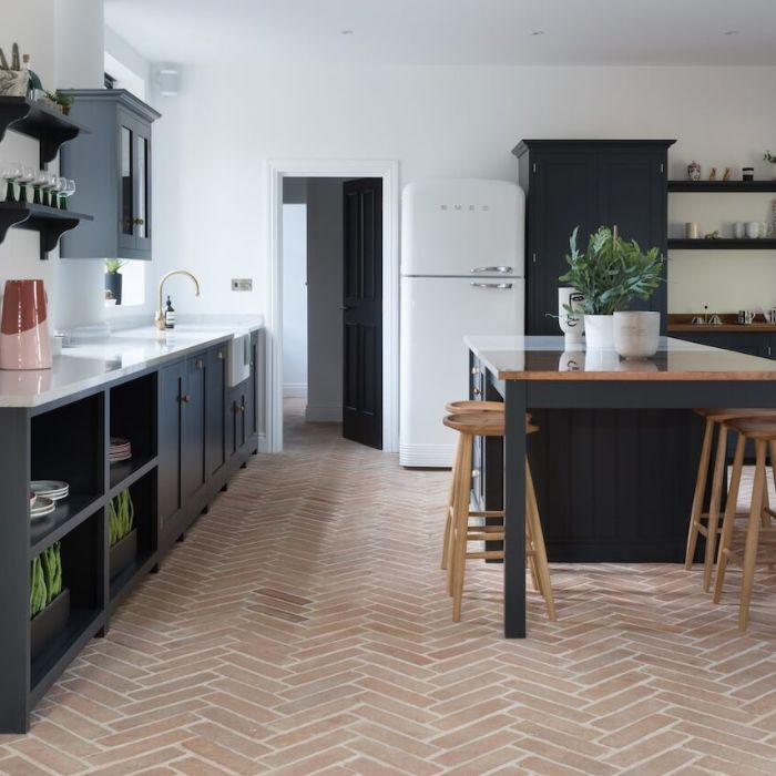 Black cabinets contrast against elegant herringbone terracotta floor tiles in a stylish kitchen