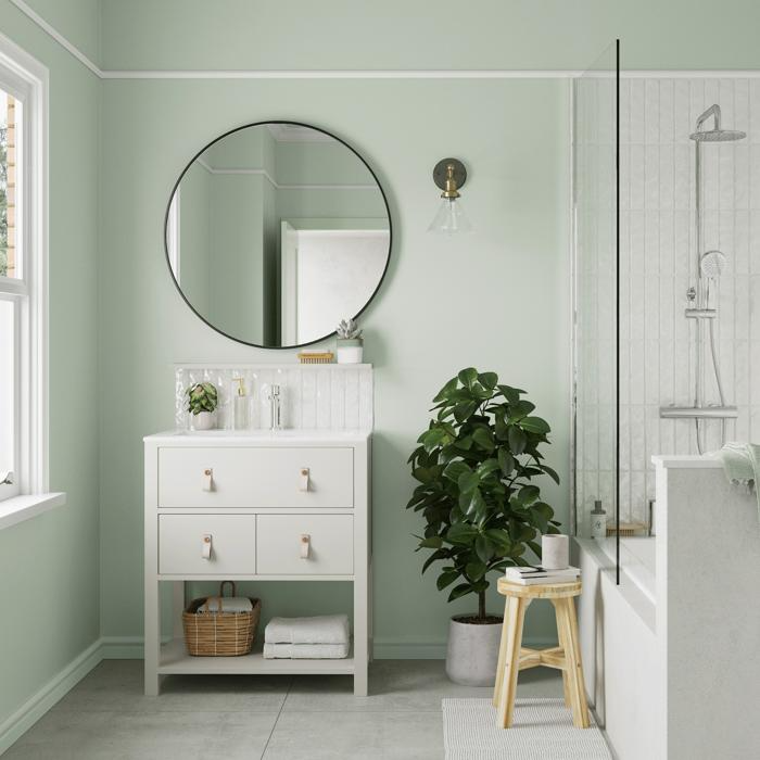 Light green bathroom with a round mirror and white vanity