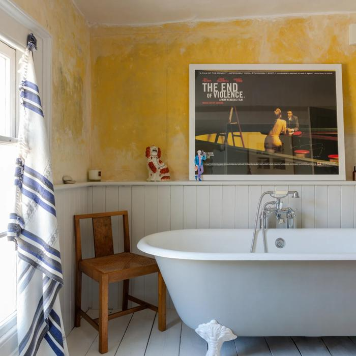 Yellow distressed wall and white clawfoot bathtub with wood accents