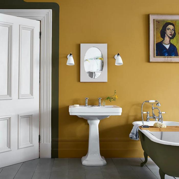 Mustard yellow walls with a white pedestal sink and framed artwork