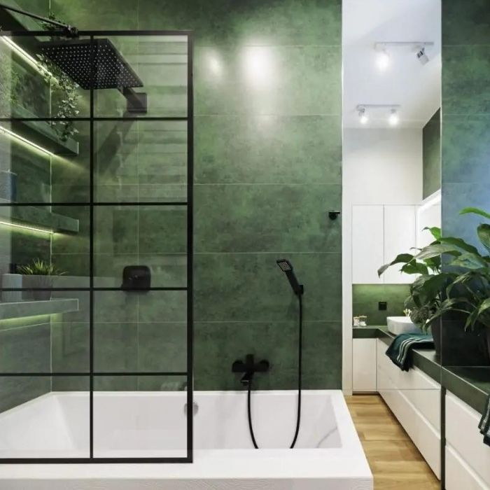 Bathtub with black fittings in green tiled bathroom