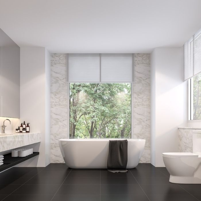 Large window with marble tiles around freestanding bath