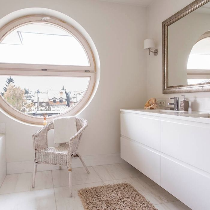 Round window in a bright white bathroom with wicker chair