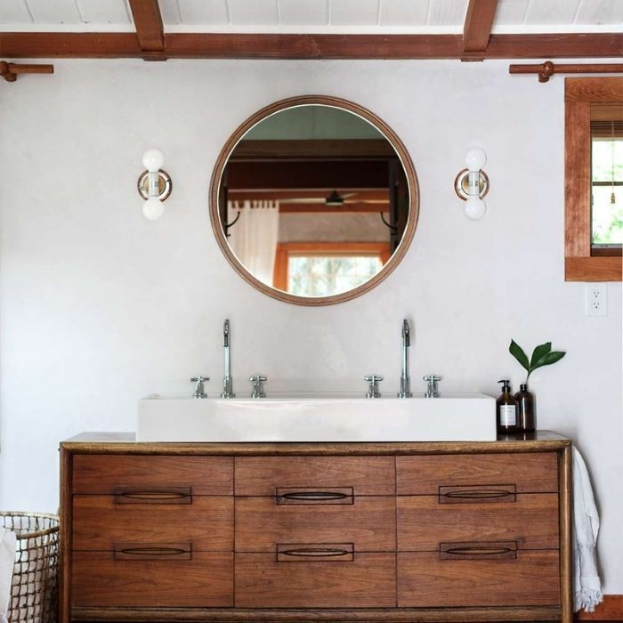 Bathroom with wooden vanity and round mirror on white wall