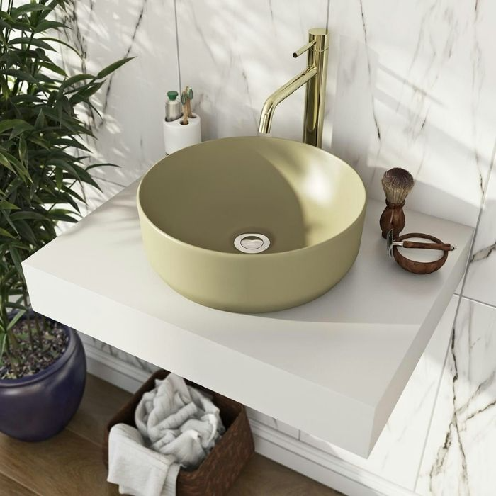 Round green sink with brass tap and marble wall