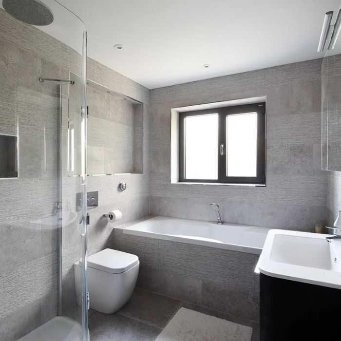 Grey stone tiles in sleek family bathroom with curved glass shower