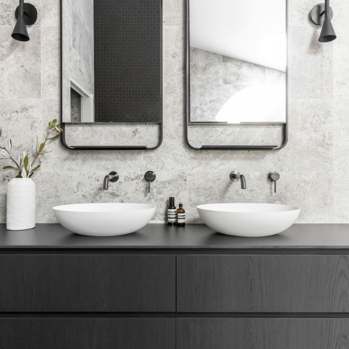 Black vanity with white sinks against grey tiled walls