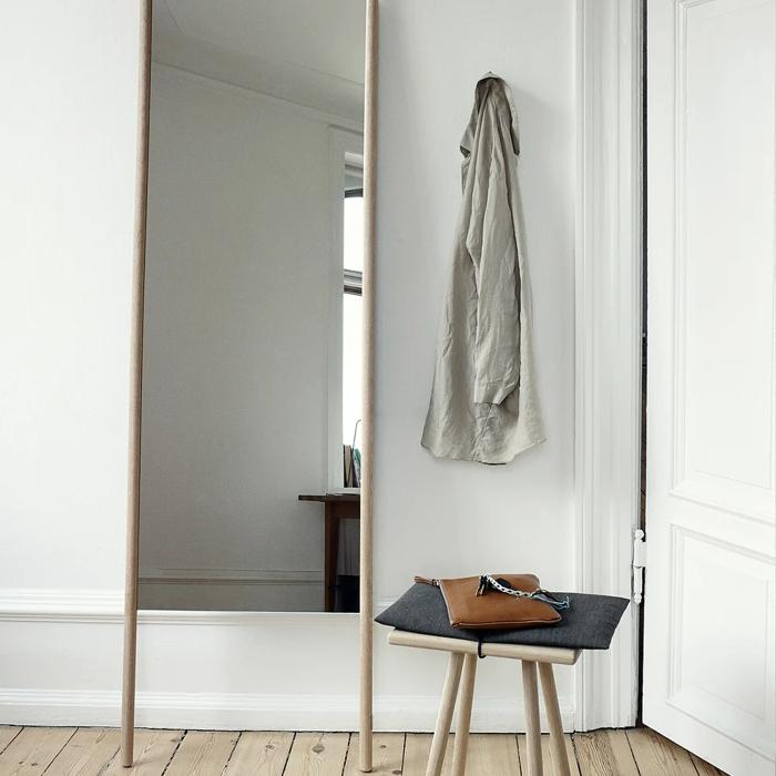 Minimalist entryway with wooden floor mirror leaning against a white wall