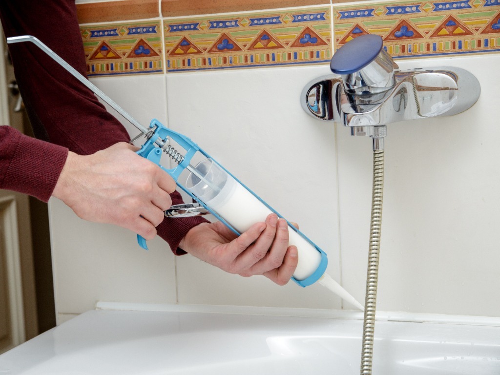 Applying silicone sealant around bathtub faucet for waterproofing.