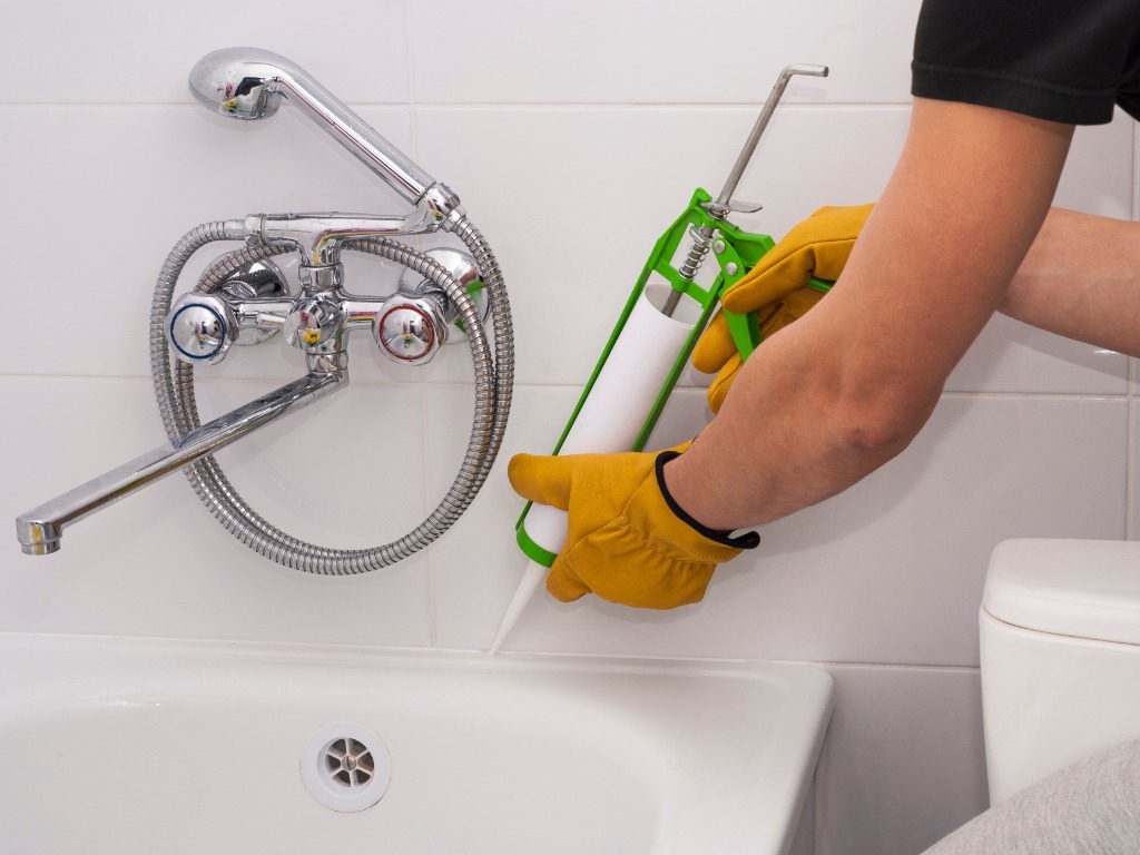 Applying silicone sealant around bathtub for waterproofing and protection.