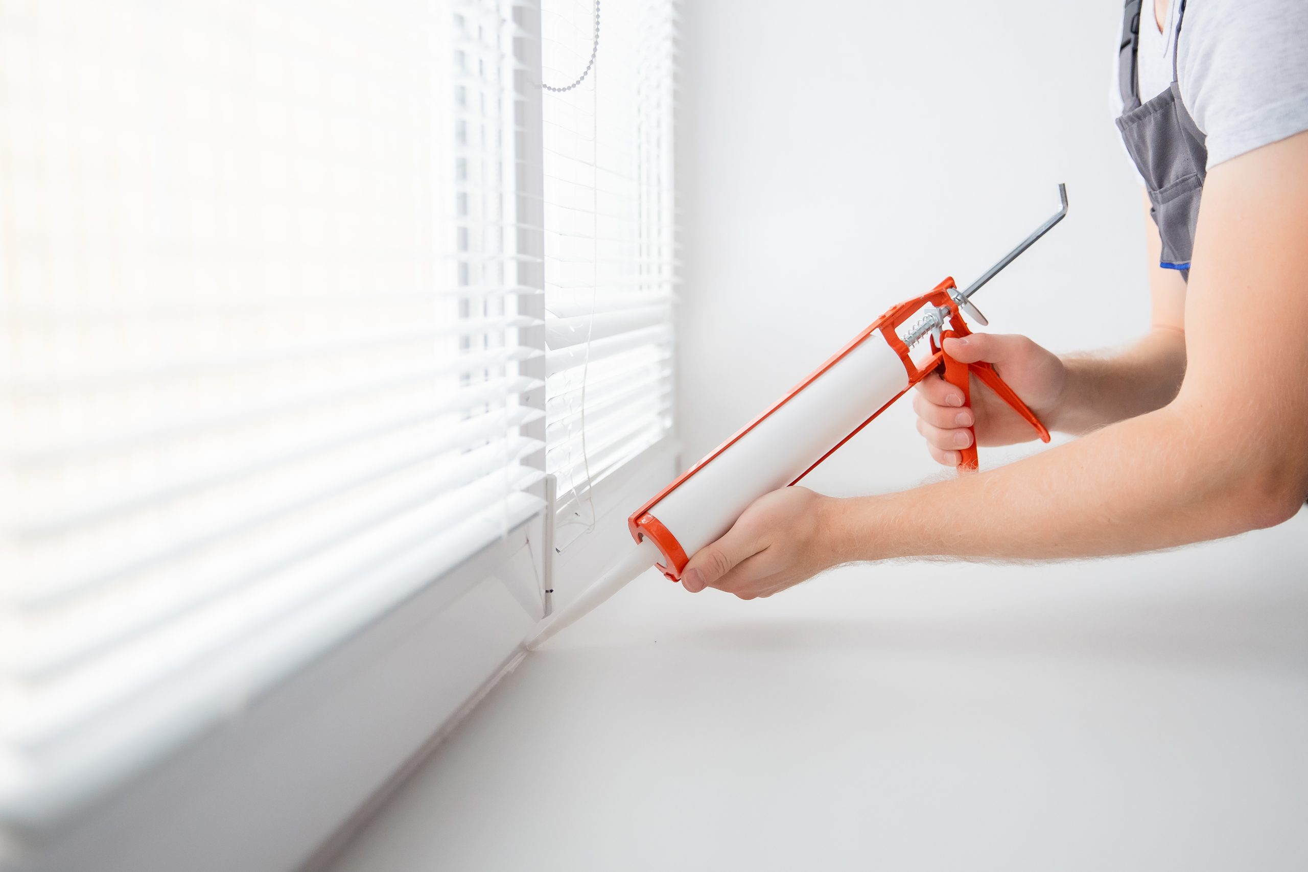 Applying silicone sealant using a caulking gun in bathroom.