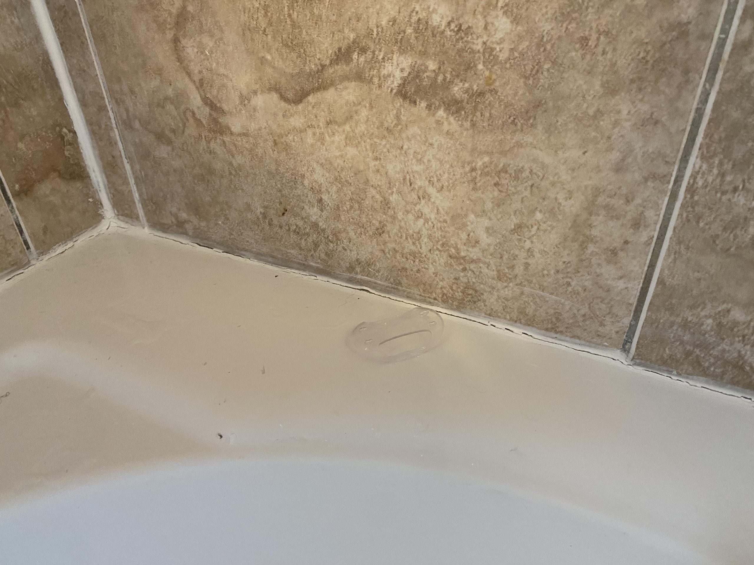 Freshly applied silicone in bathroom corner with drying edges.