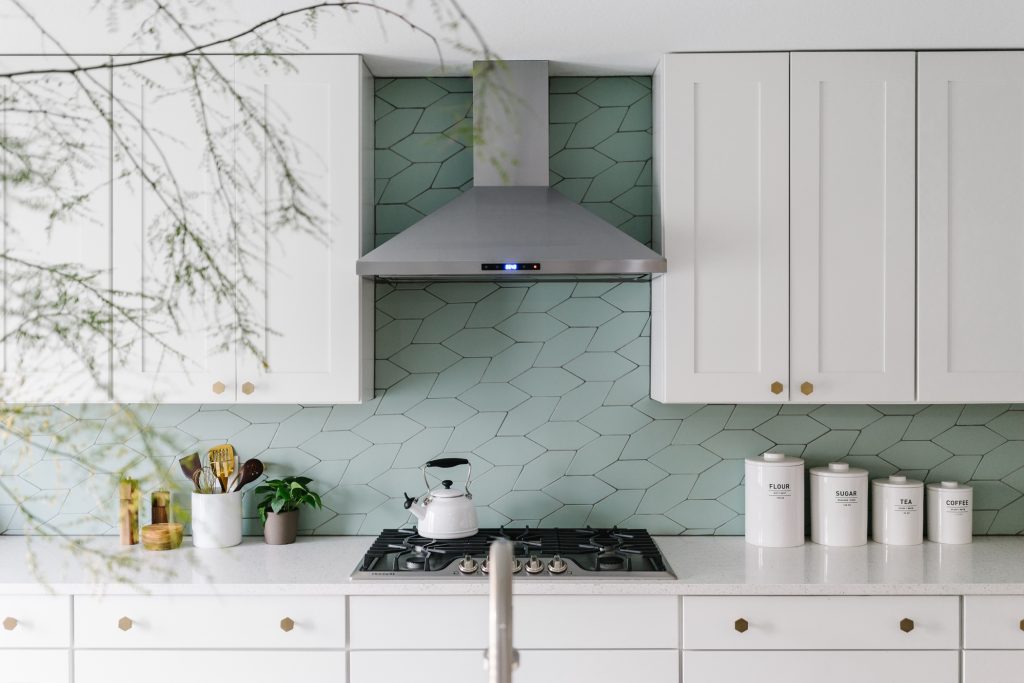 Sage green geometric tiles complement sleek white kitchen cabinets beautifully.