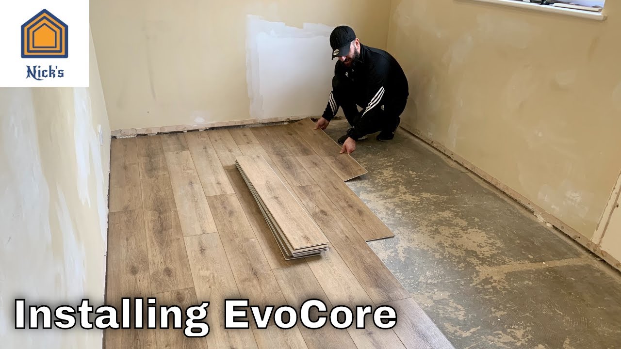 Worker installing Evocore flooring in an unfinished room.