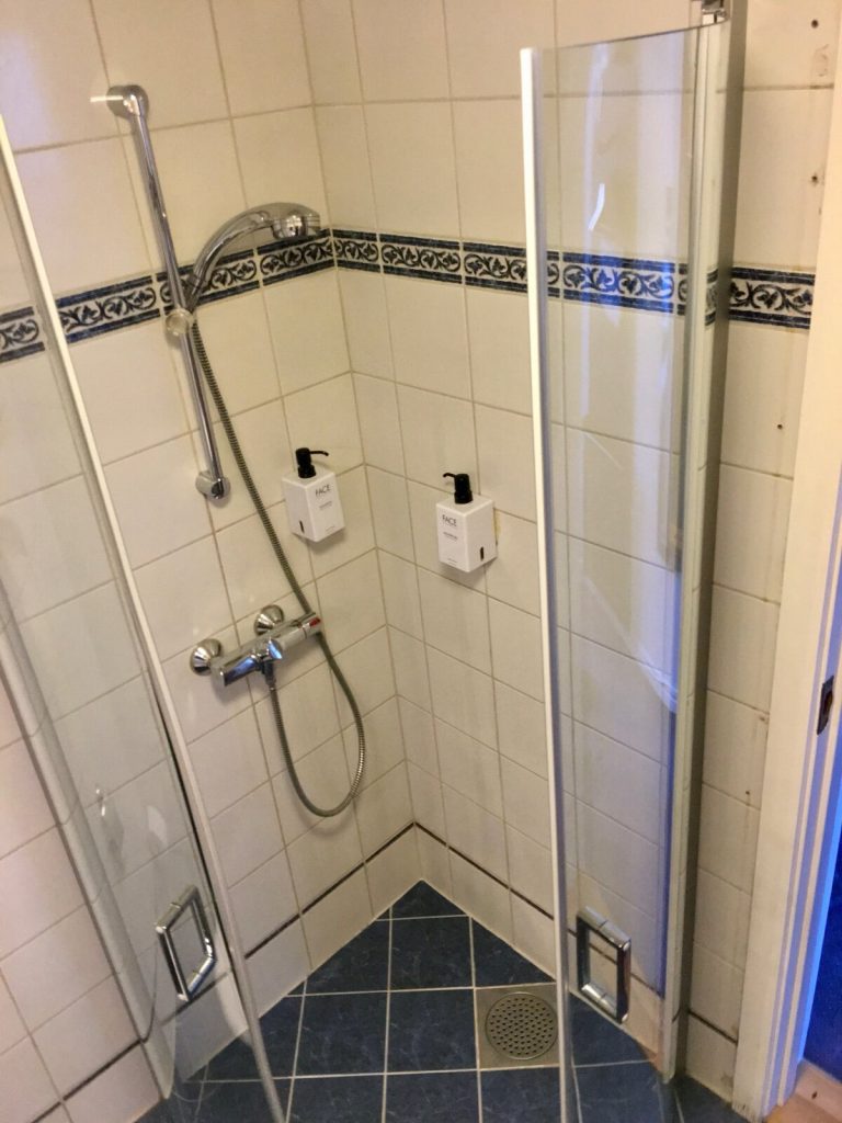 Tiled bathroom wall with chrome shower valve and pipework passing through the tiles