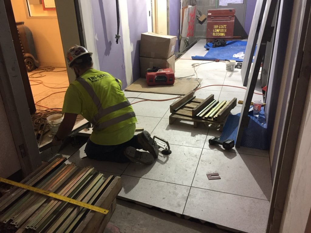 A tiler kneeling to lay large format floor tiles on a prepared substrate