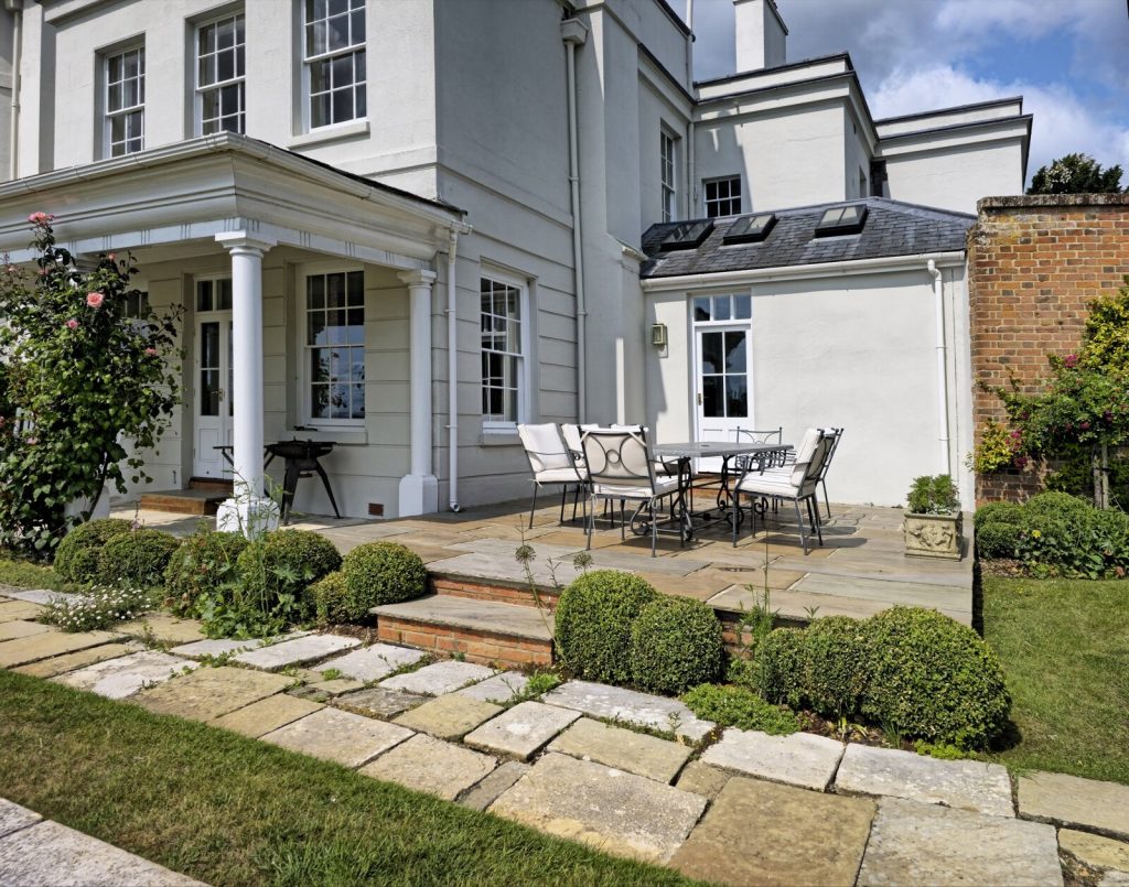 A laid stone patio running alongside a rendered house, with a step down to an older paved path