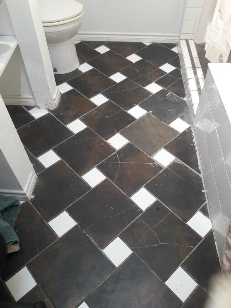 Cracked dark slate floor tiles in a bathroom, with splits running across several tiles