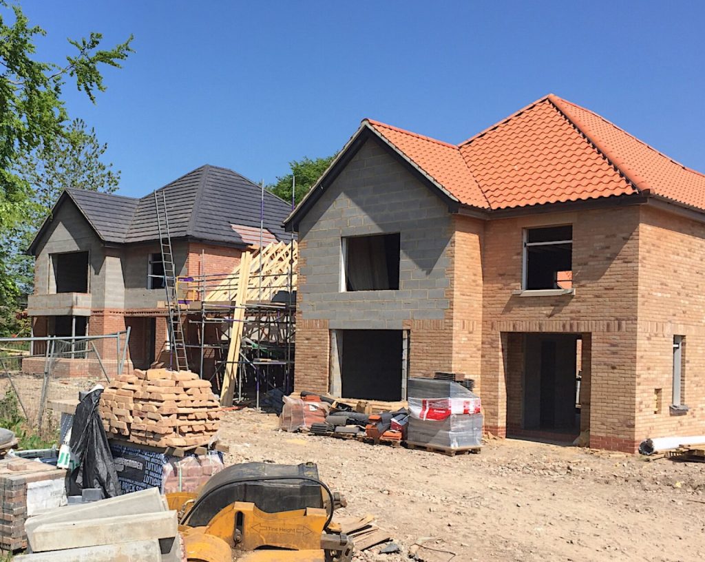 New houses under construction with scaffolding, roof tiles and stacked bricks on a UK building site