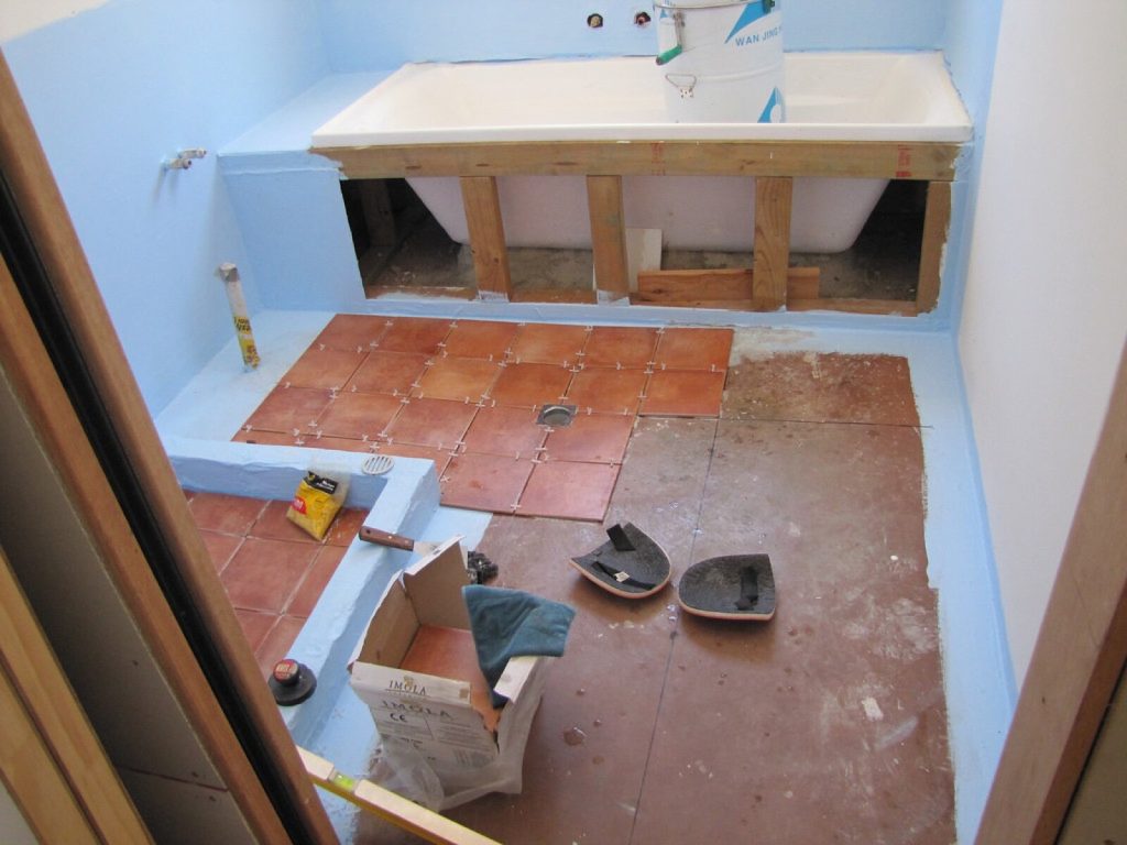 Bathroom floor being tiled, with tile adhesive, a notched trowel and a spirit level
