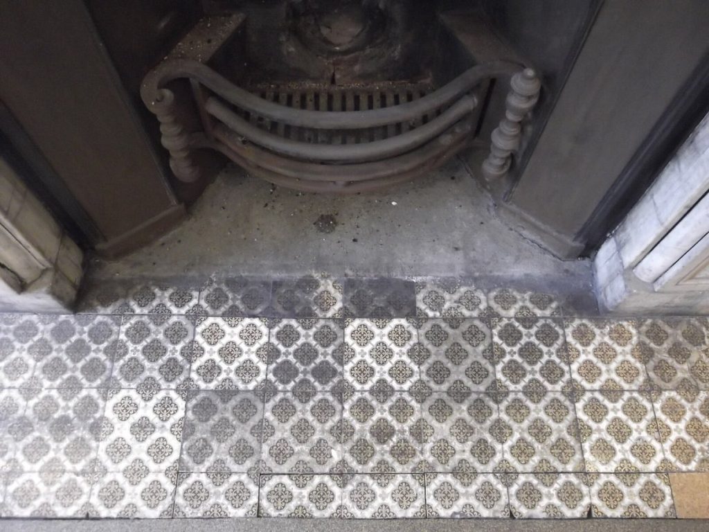 Patterned grey and white tiled hearth in front of a cast iron fire grate