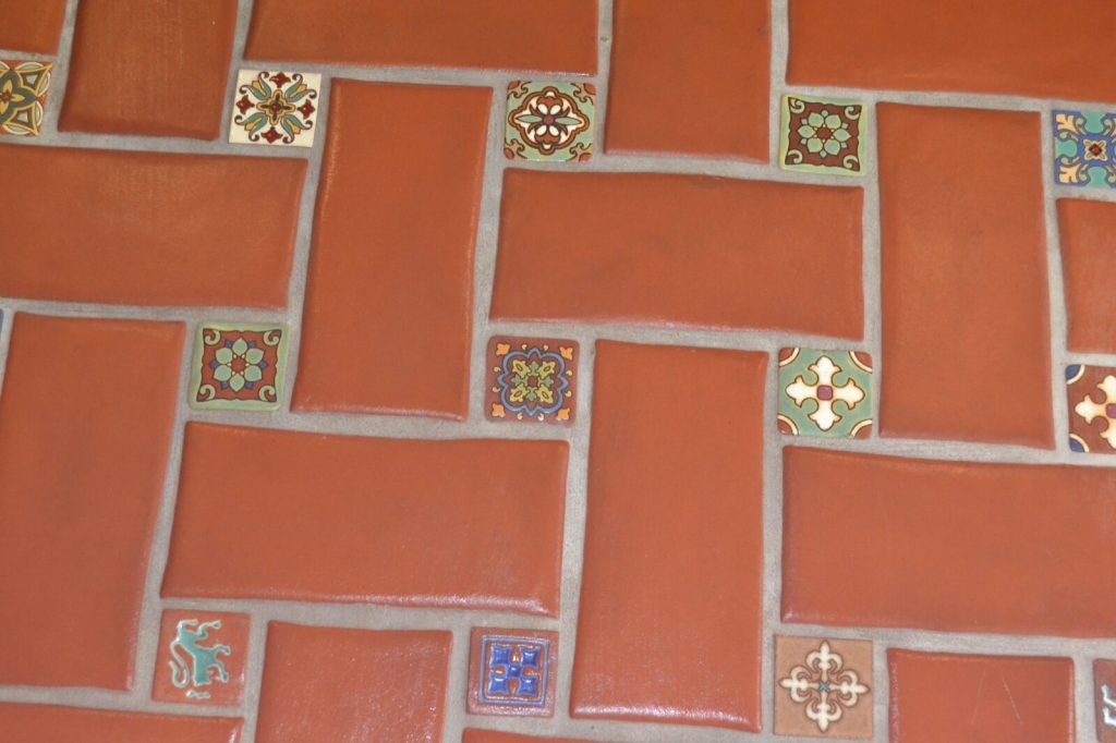 Red terracotta floor tiles laid in a mixed running bond with small decorative glazed inserts