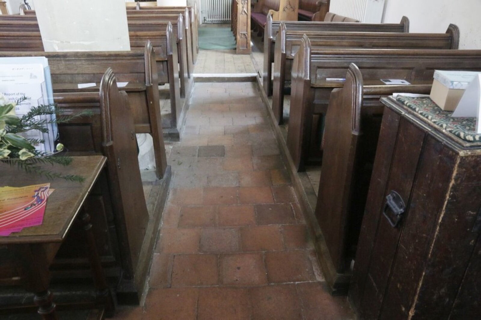 A worn red quarry tile floor running down a church aisle between wooden pews