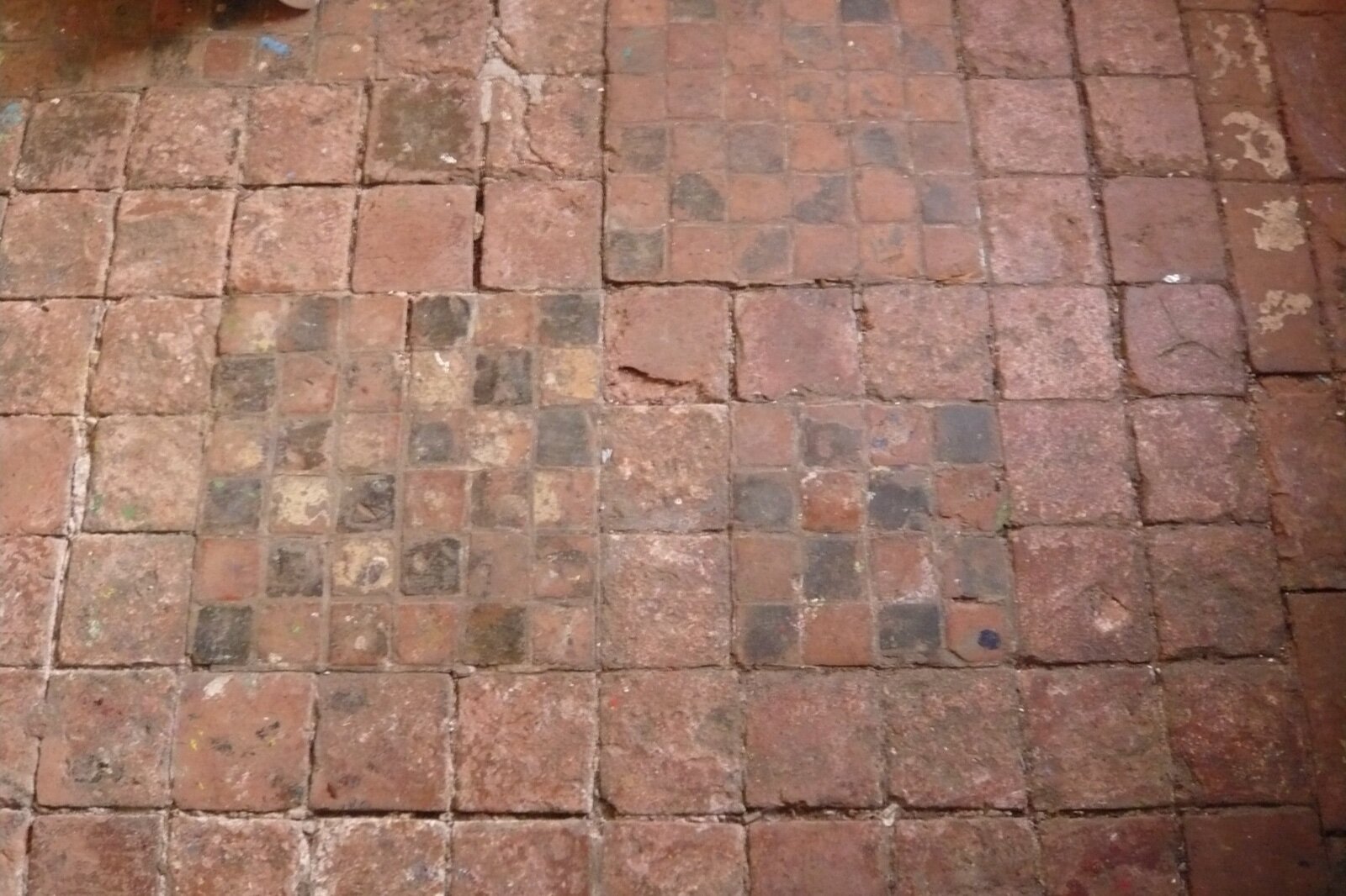 A 16th century unglazed clay tile floor, heavily worn, with paint marks and staining across the tiles