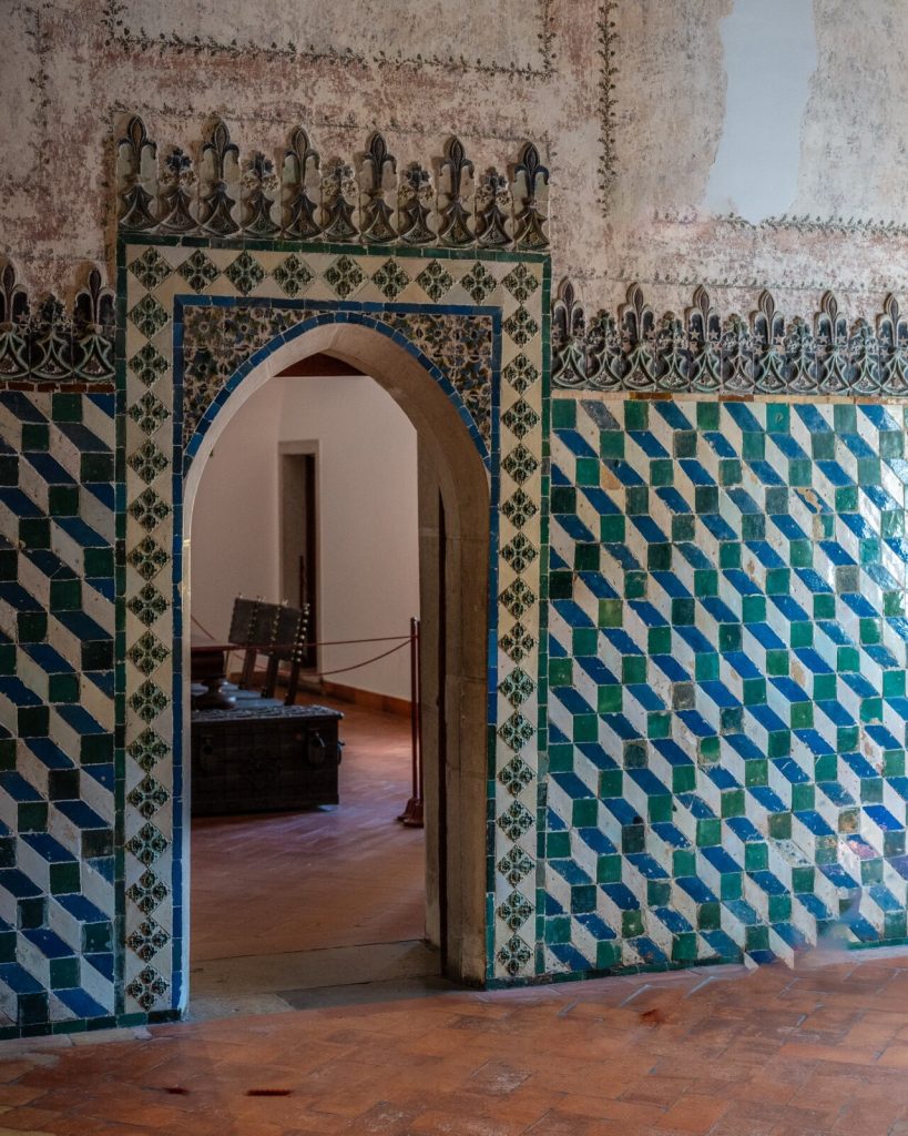 A wall covered in patterned blue and green geometric tiles beside a tiled archway