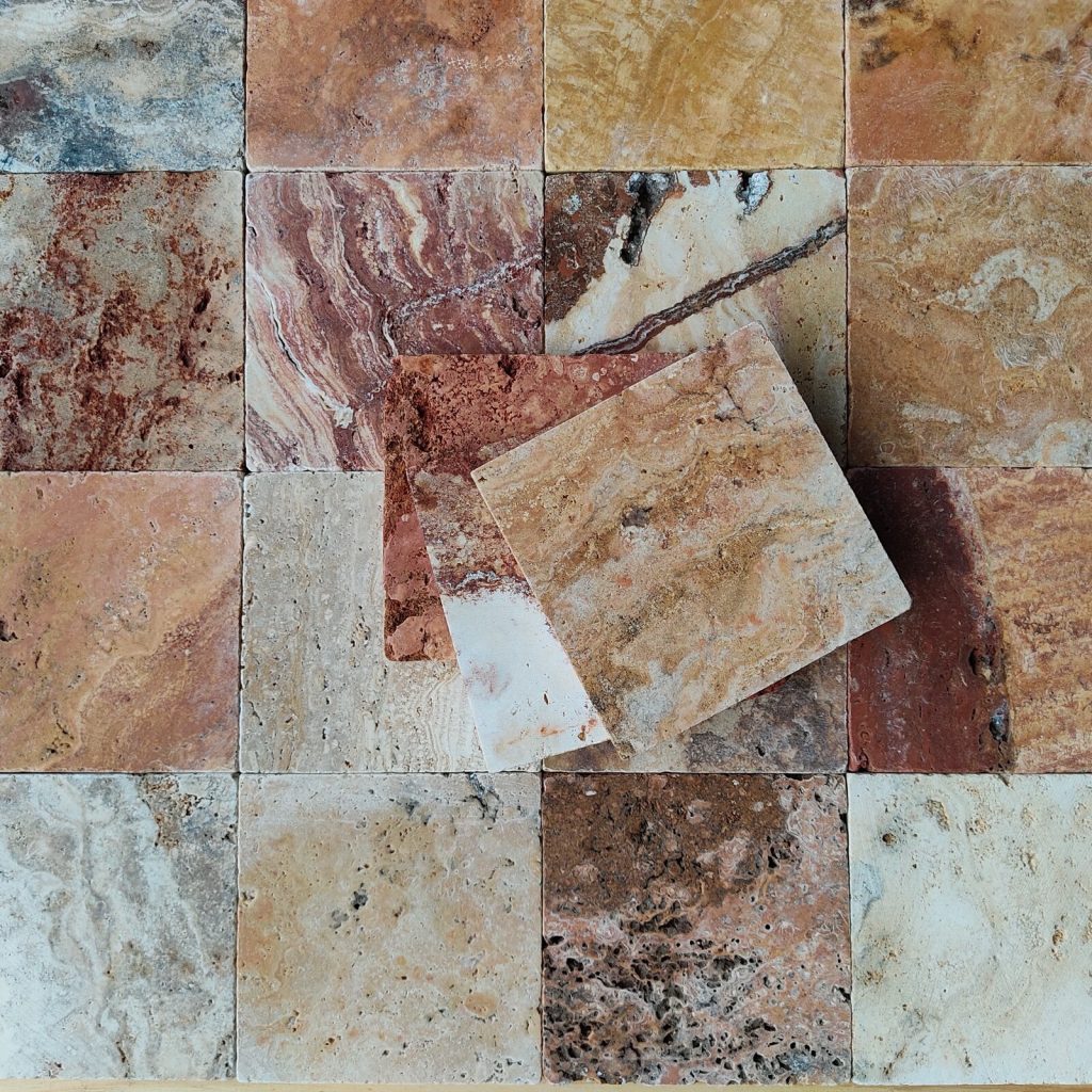 Tumbled travertine tiles in cream, gold, red and grey laid in a grid, showing the natural pores and veining
