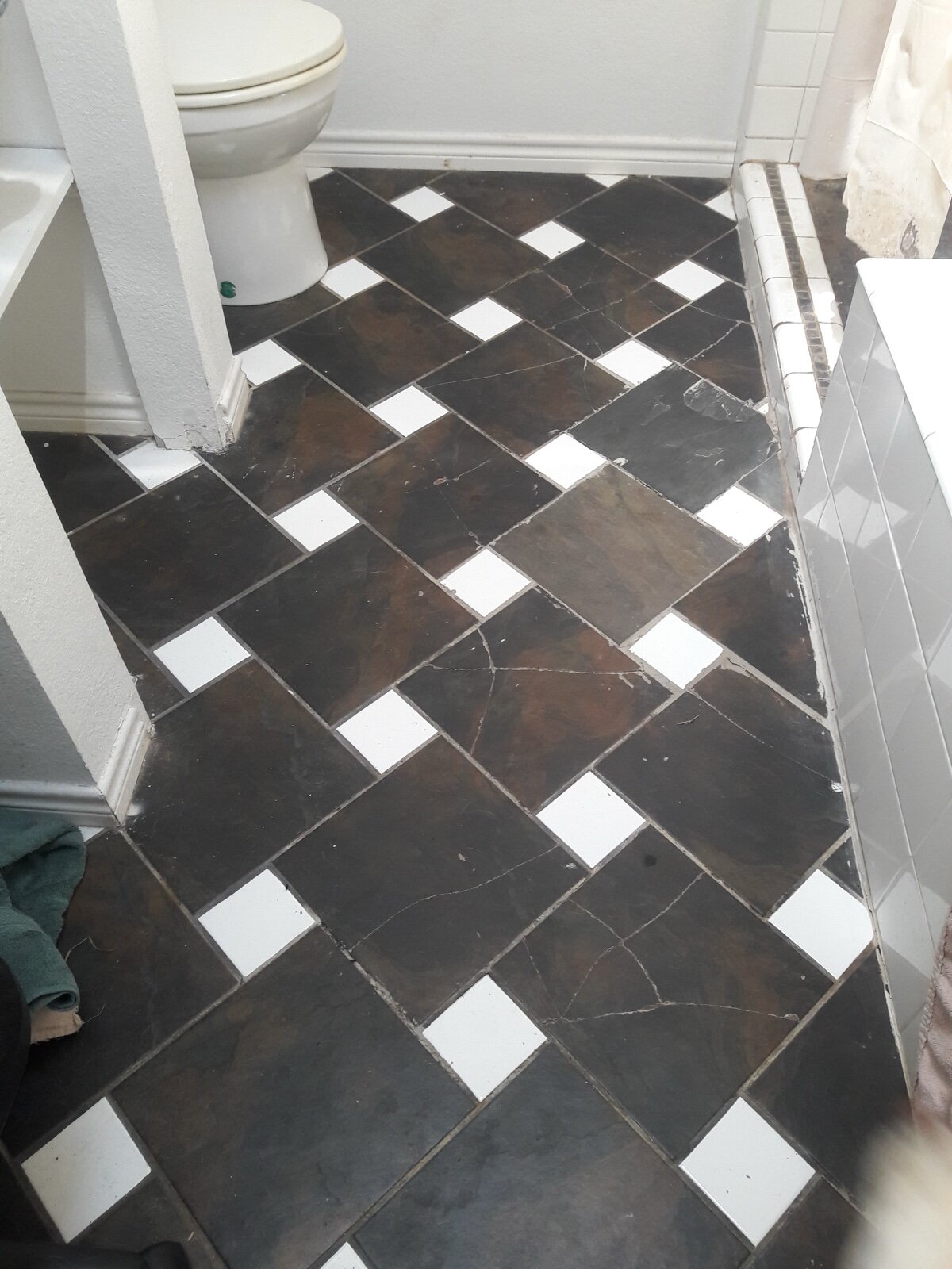 Cracked dark floor tiles laid diagonally in a small bathroom