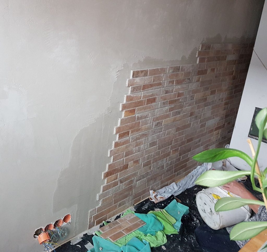 Brick-effect porcelain wall tiles part-way through fixing on a smooth plastered wall