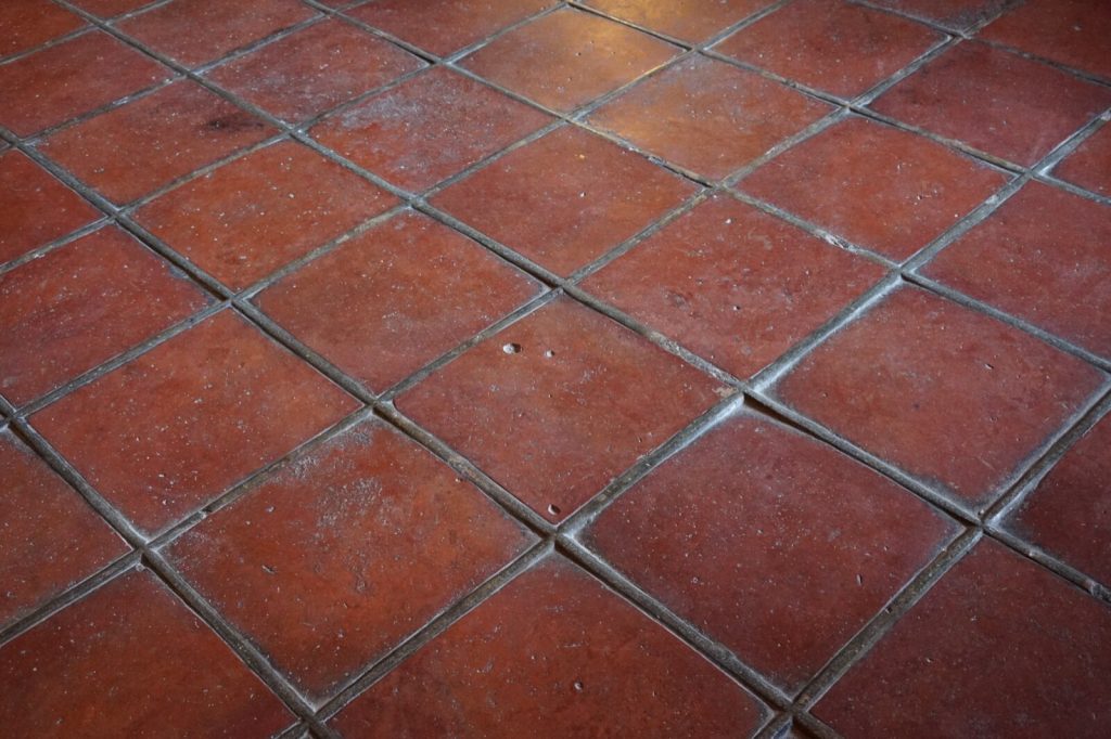 Square terracotta floor tiles laid on the diagonal with grey grout joints