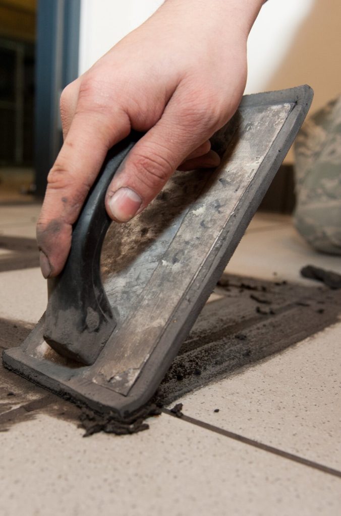 Grout being spread across floor tile joints with a rubber float