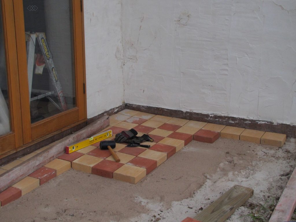 Outdoor floor tiles being laid outside a glazed door with a spirit level