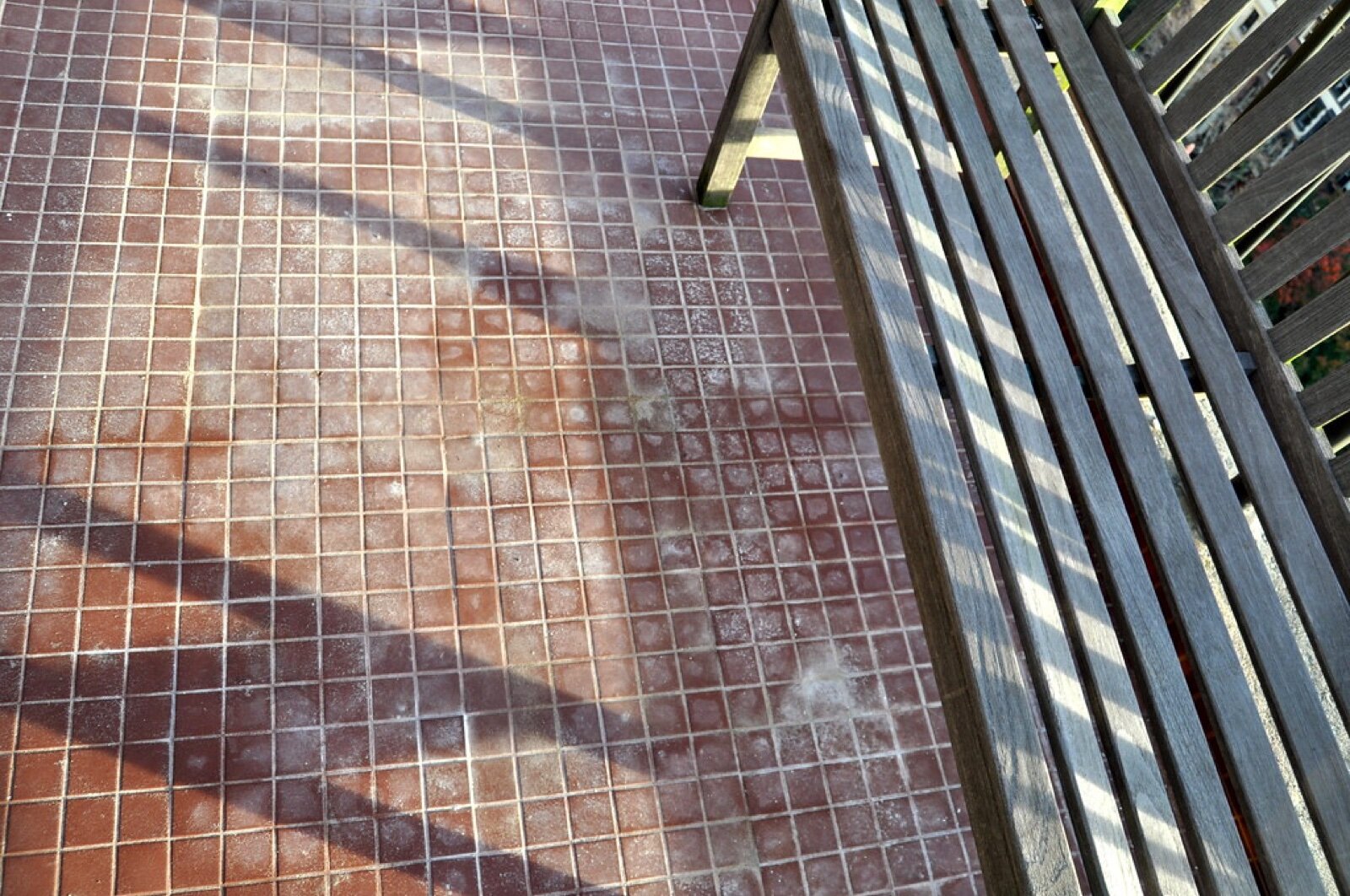 Terracotta mosaic tiles on a balcony floor beside a slatted rail