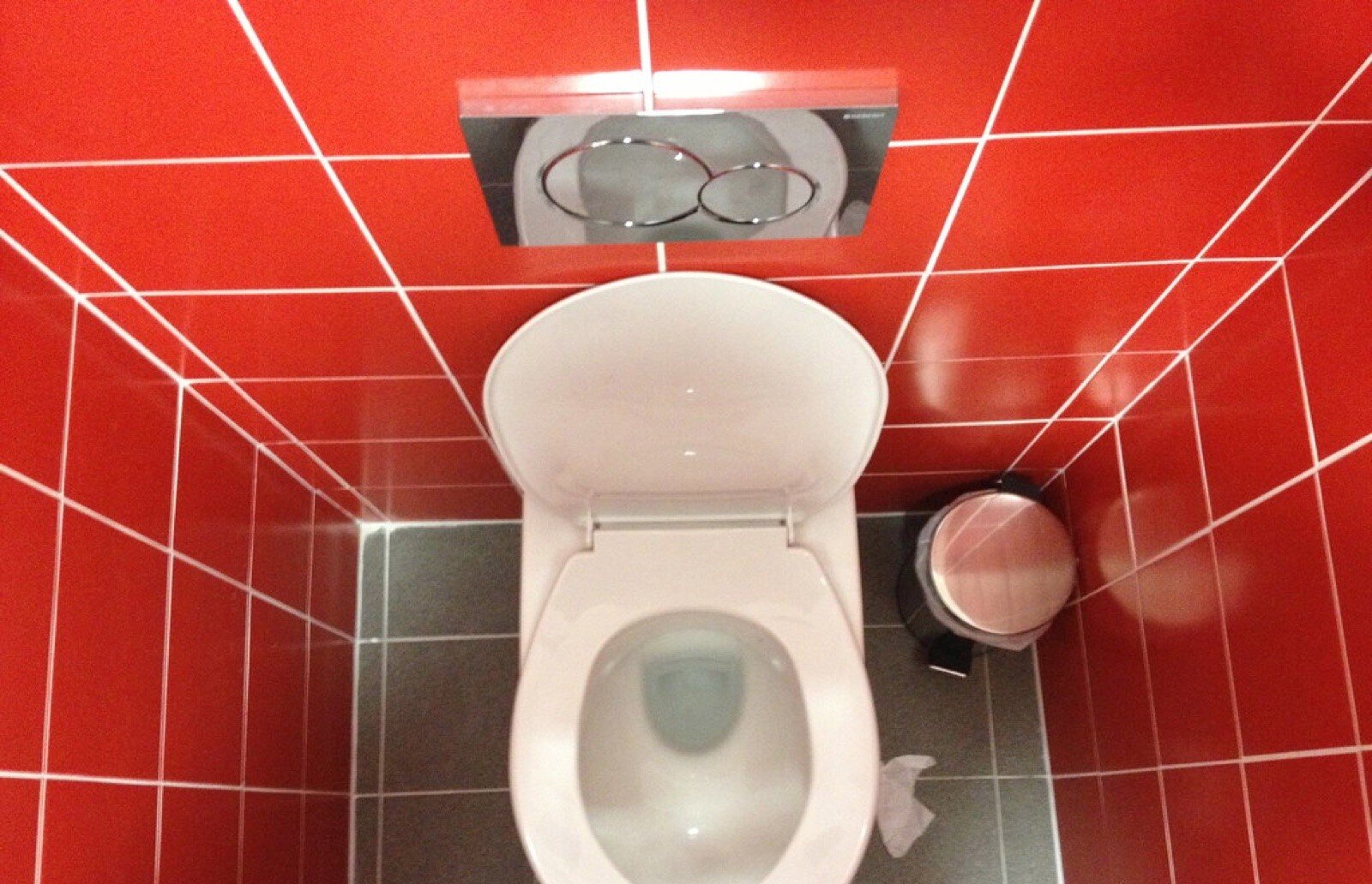Concealed cistern flush plate set into red wall tiles above a white toilet pan