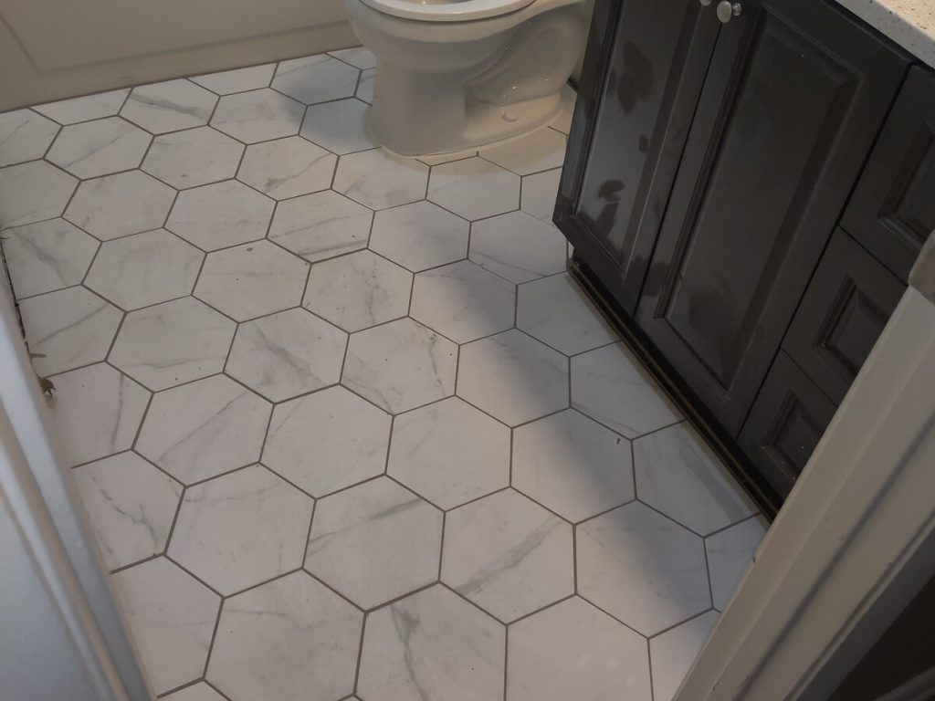 A bathroom floor laid in large white marble-effect hexagon tiles beside a dark vanity unit
