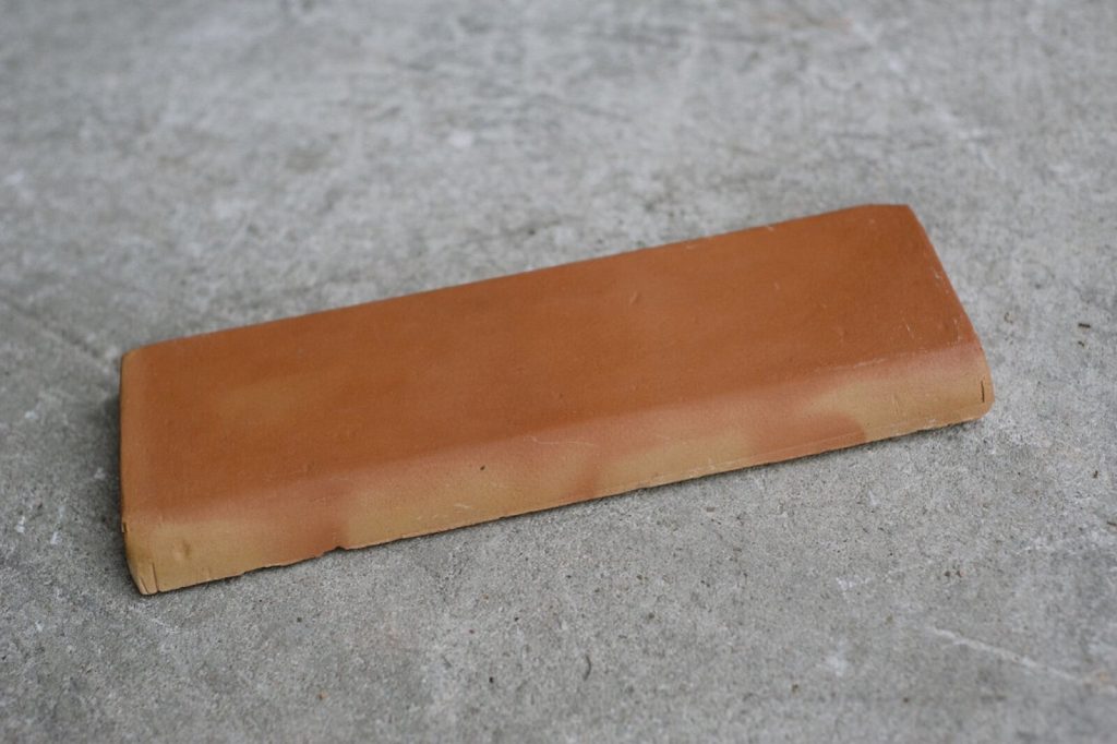 A terracotta bullnose tile with a rounded top edge lying on a grey surface