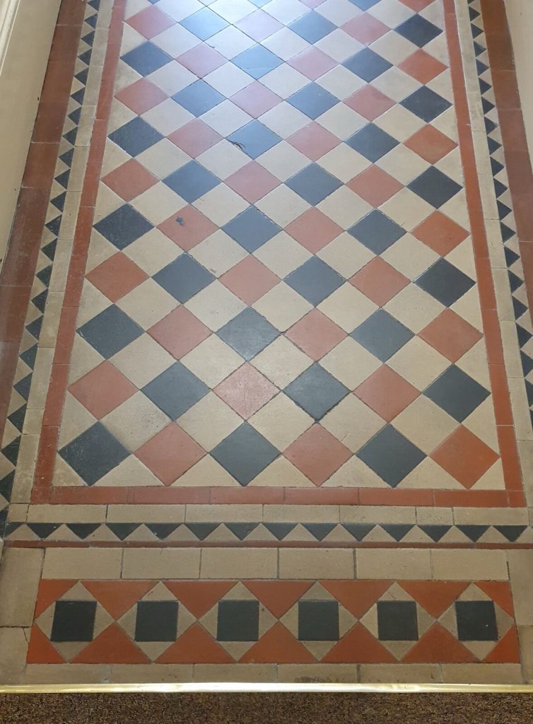 Geometric hallway floor tiles finishing at a brass strip against carpet